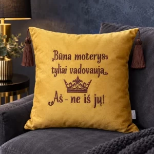 Garstyčių spalvos dekoratyvinė pagalvėlė su siuvinėtu užrašu „Būna moterys tyliai vadovauja. Aš – ne iš jų!“, karūna ir tamsiais kutais