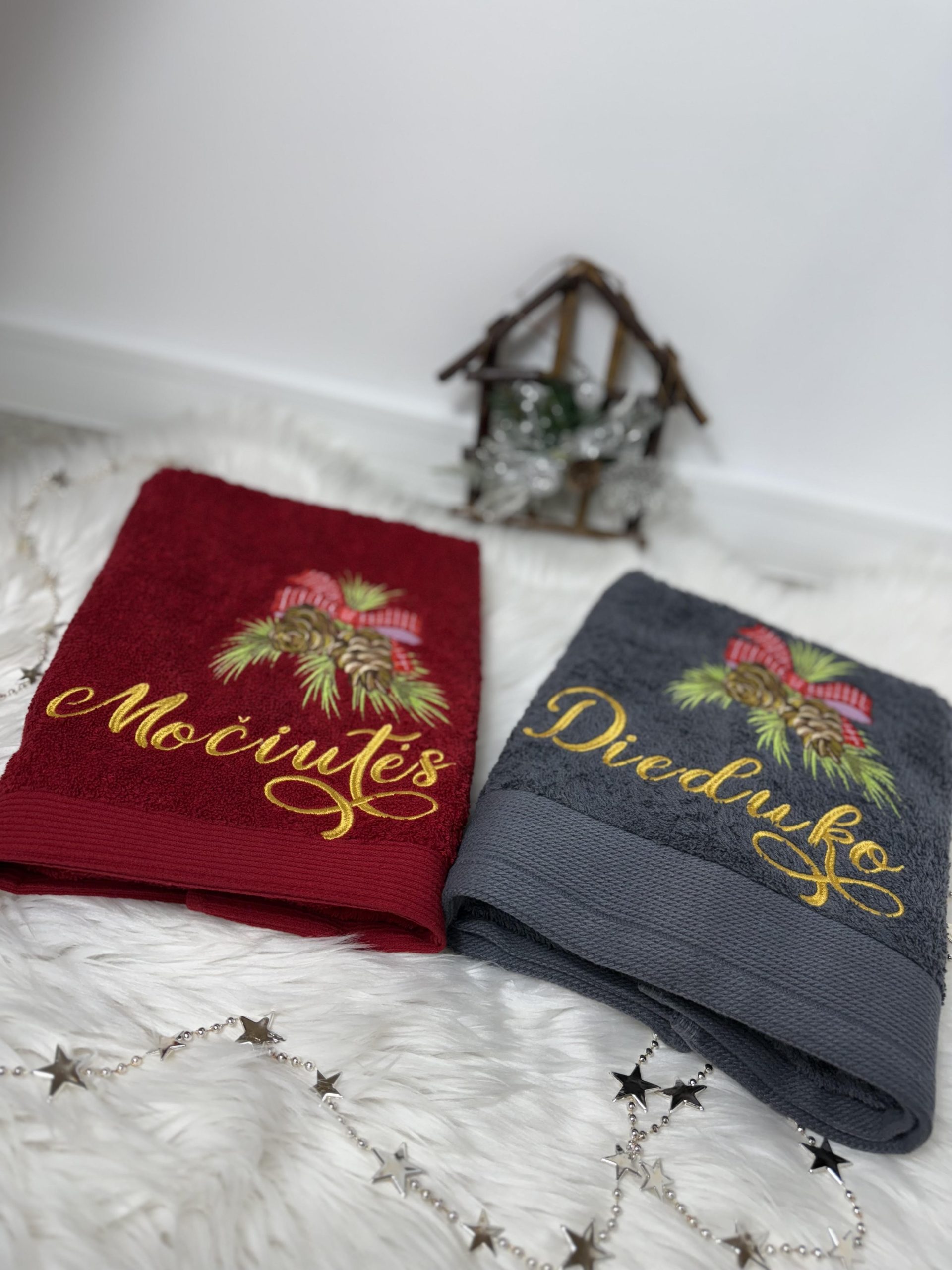 Raudonas ir pilkas siuvinėtas rankšluostis su užrašais „Močiutės“ ir „Dieduko“, puoštais eglės šakelėmis ir kankorėžiais.