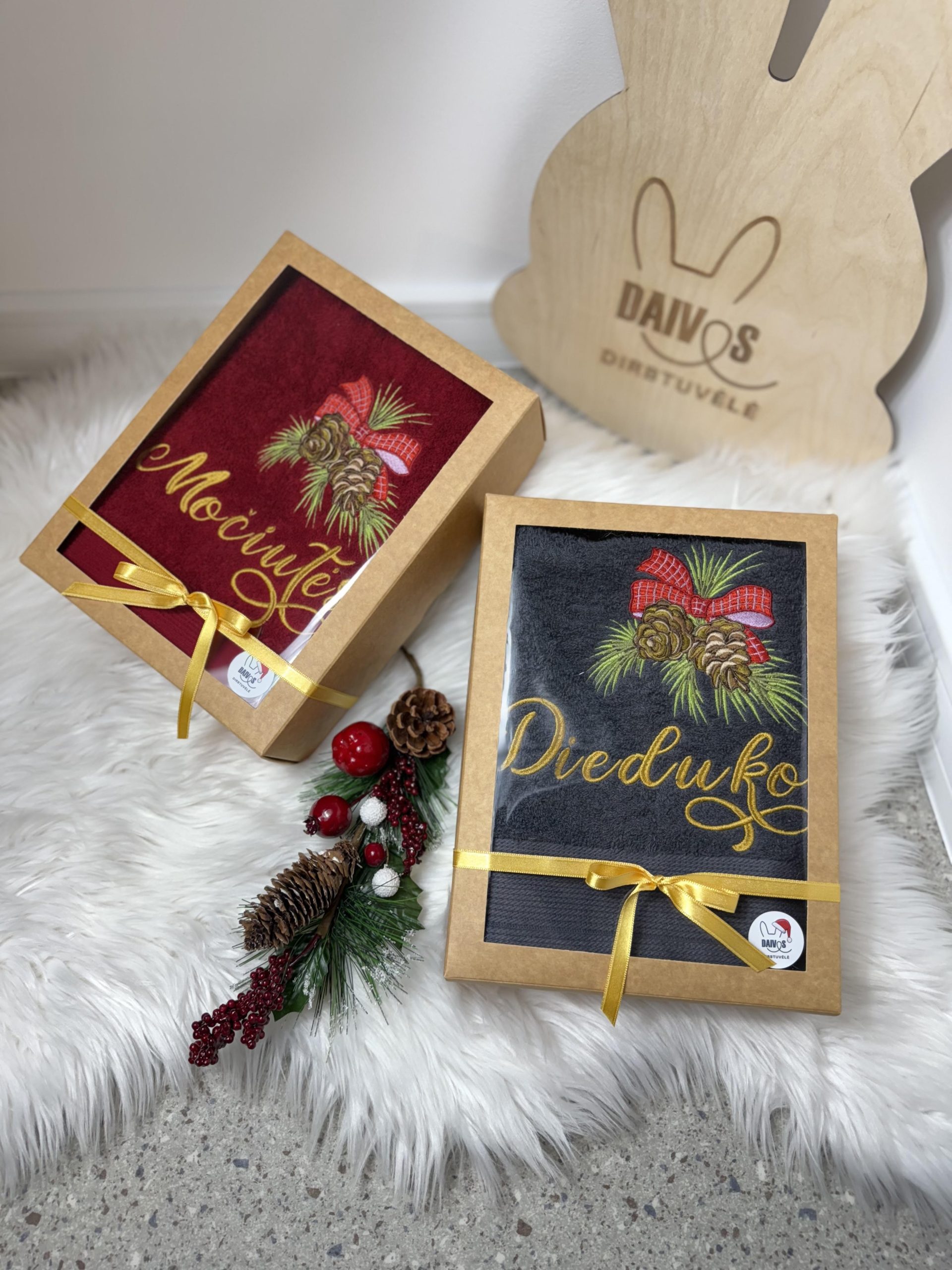 Raudonas ir pilkas siuvinėtas rankšluostis su užrašais „Močiutės“ ir „Dieduko“, puoštais eglės šakelėmis ir kankorėžiais